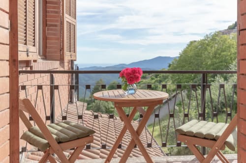 Balcon avec vue sur les montagnes à l'hôtel Allegria, Bajardo. Table en bois, fleurs roses, chaises et les Alpes en arrière-plan.