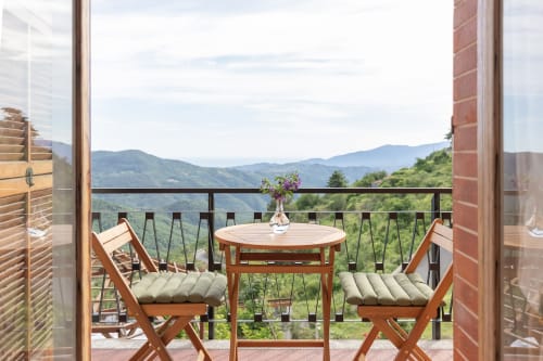 Balcon de l'hôtel Allegria à Bajardo avec chaises en bois, table, fleurs et vue sur les montagnes