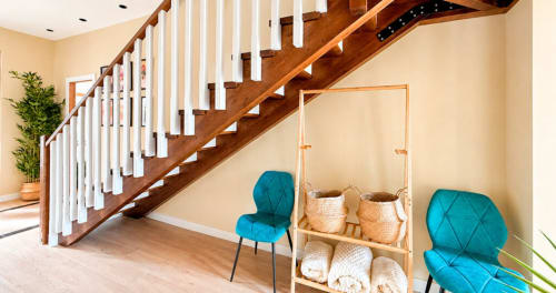 Moderno vestíbulo del hotel La Posada de las Flores con escalera de madera, sillas turquesas y cestas de almacenamiento tejidas