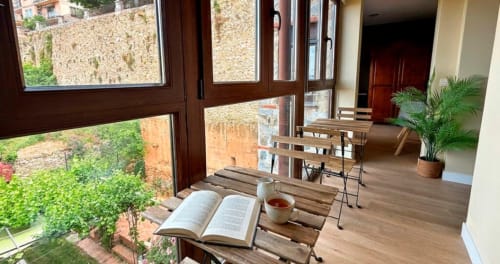 Rincón acogedor para leer en La Posada de las Flores con libro abierto, té y vistas al jardín a través de puertas de madera