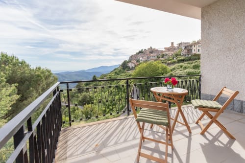 Balcon avec chaises et table en bois offrant une vue sur les montagnes et le village de Bajardo à l'hôtel Allegria, Italie