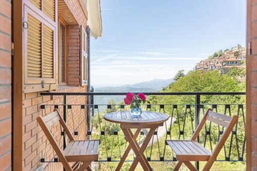 Balcon de l'hôtel Allegria à Bajardo avec chaises en bois, table de fleurs rouges et vue sur la vallée