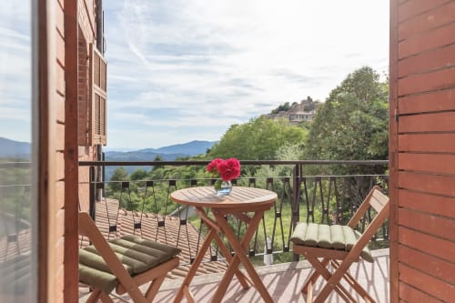 Balcon de l'hôtel Allegria à Bajardo avec mobilier en bois, fleurs roses et vue sur les montagnes