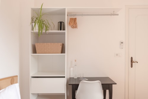 Chambre minimaliste moderne à l'hôtel Allegria à Bajardo avec étagères blanches, plante en pot, bureau foncé et chaise en bois