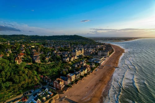 Vue aérienne de l'hôtel Skol In Normandy avec plage de sable, mer et charmante ville côtière verdoyante