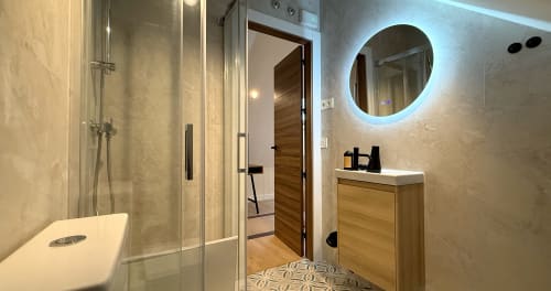 Baño moderno del hotel La Posada de las Flores en Astorga con espejo redondo iluminado, tocador de madera y ducha de cristal