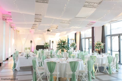 Elegant wedding reception at Château ERIGOYE with round tables, green chair sashes, and floral centerpieces in
