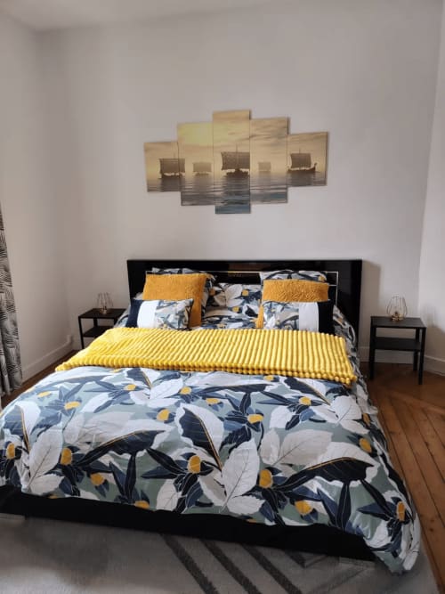 Chambre à Skol In Normandy avec literie fleurie, accents jaunes et décor maritime au-dessus du lit noir