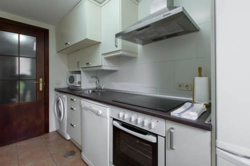 Cocina moderna en apartamento La Cabrera con muebles blancos, encimera negra, horno, lavadora y campana acero inoxidable