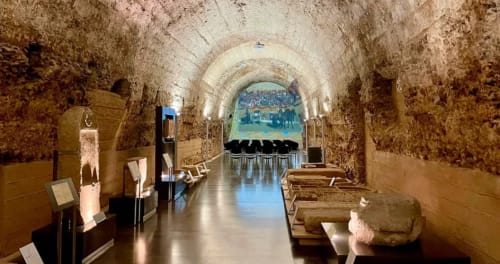 Pasillo histórico abovedado de piedra en La Posada de las Flores de Astorga con exposiciones de museo y zona de descanso.