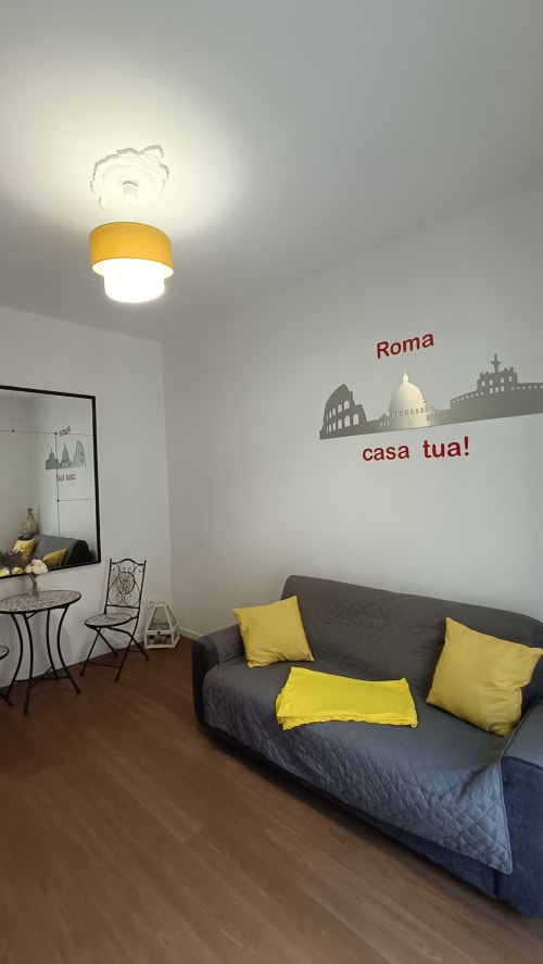 Divano grigio con cuscini gialli nell'appartamento Roma Casa Tua, con lampada a soffitto e decorazione murale con skyline di Roma