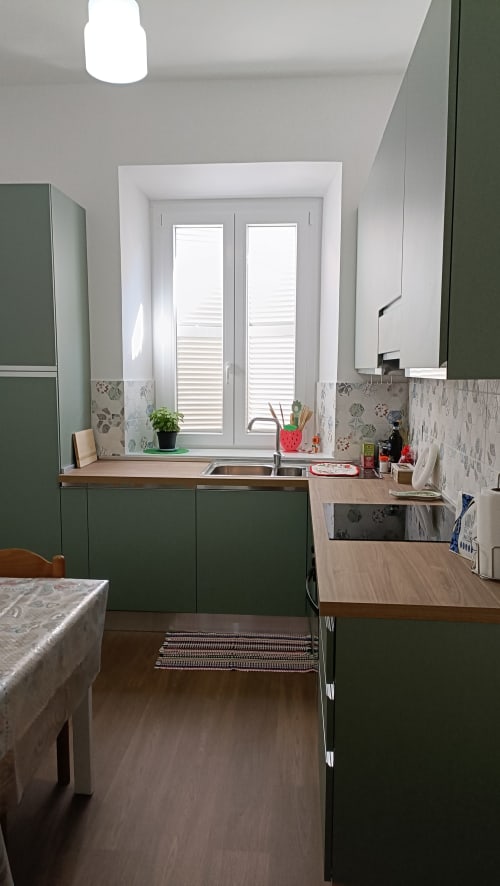 Cucina moderna verde nell'appartamento Roma Casa Tua con lavello, piani in legno e porte finestre con scuri