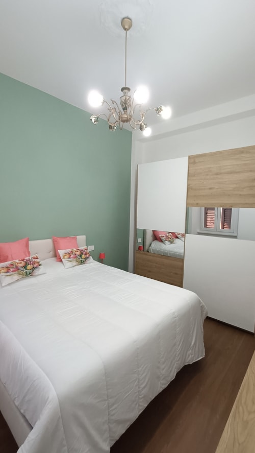 Camera da letto Annarella Maison a Roma Casa Tua con pareti verde menta, letto bianco, armadio specchiato e lampadario decorativo
