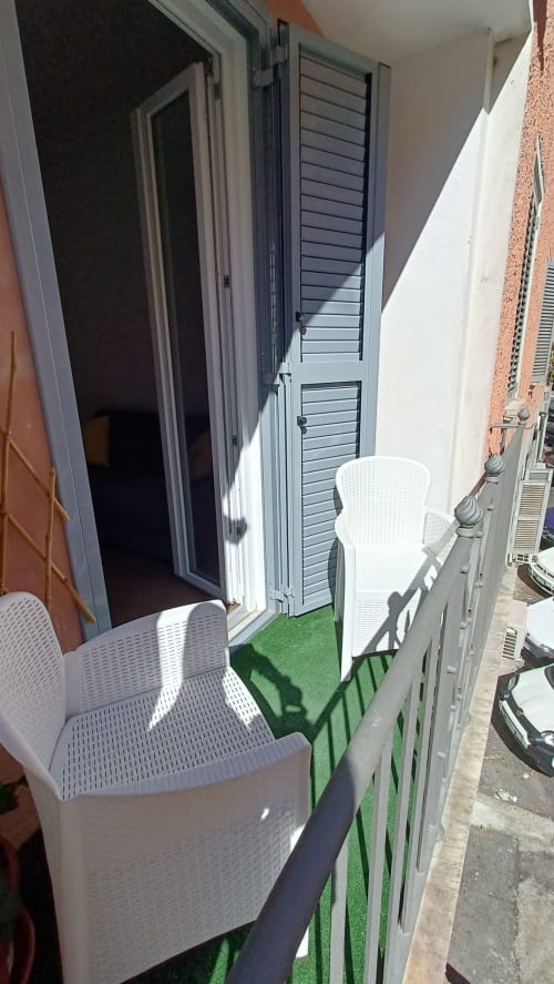 Balcone compatto a Roma Casa Tua con sedie bianche e pavimentazione verde artificiale, affacciato sulla strada cittadina