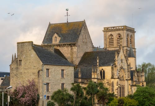 Église en pierre historique avec tour en Normandie, France. Architecture gothique avec croix et palmiers.