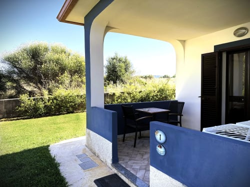Villetta 1, patio con pergolato azzurro, arredi neri, giardino curato e vista sul mare a Valledoria