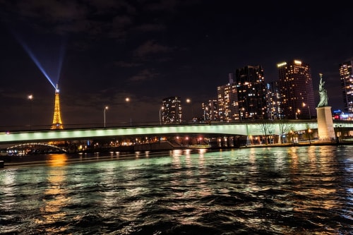 Vue nocturne de la Seine à Paris avec la tour Eiffel illuminée, pont éclairé, réplique de la Statue de la Liberté et skyline urbain