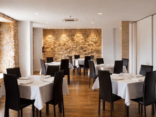 Elegante comedor del Hostal Doña Blanca en Sigüenza con paredes de piedra, mesas redondas con manteles blancos y sillas negras