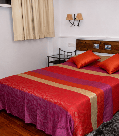 Habitación estándar del Hostal Doña Blanca en Sigüenza con ropa de cama colorida, cabecero de madera y cortinas beige