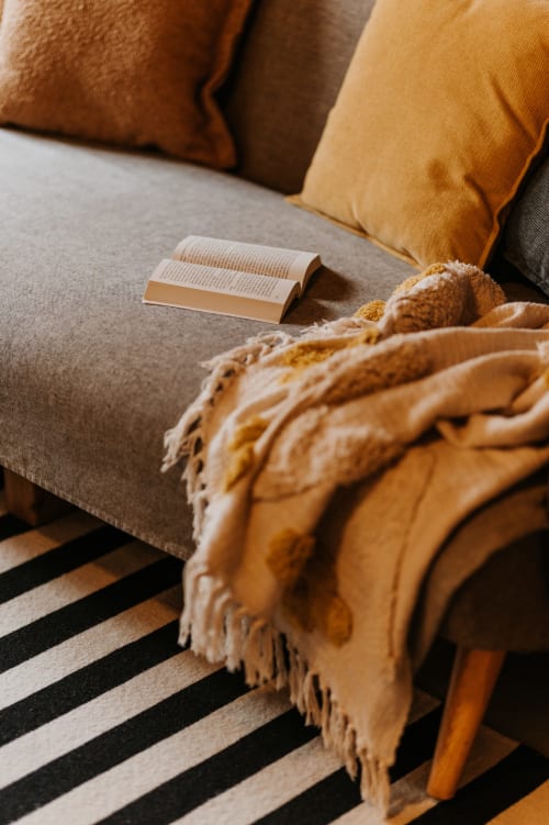 Coin lecture confortable au gîte La Grange Mimosa avec livre, coussins moutarde et plaid douillet aux Granges De Pil Bara,