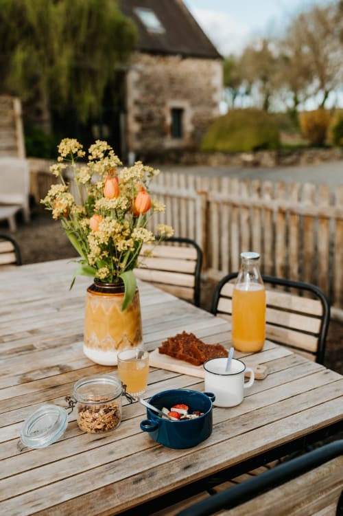 Table de petit-déjeuner en plein air aux Granges De Pil Bara avec fleurs, jus et vue sur la campagne à Langoat, France