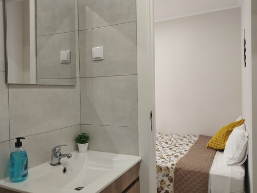 Modernes Badezimmer mit grauen Fliesen, weißem Waschbecken und Spiegel in der Furnaka Village Herberge in Lourinhã, Portugal, mit Blick auf das Schlafzimmer
