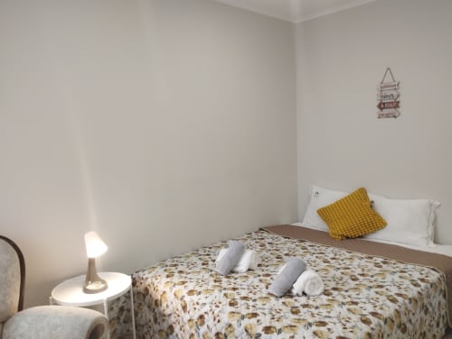 Gemütliches Zimmer in der Furnaka Village Herberge in Lourinhã mit blumiger Bettdecke, gelbem Kissen, weißen Kissen und Nachttischlampe