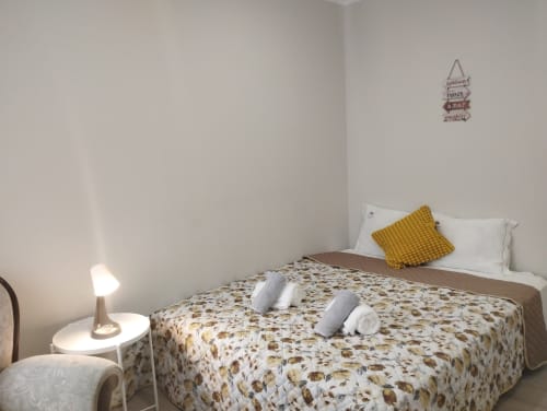 Helles Schlafzimmer in der Furnaka Village Herberge in Lourinhã mit gemustertem Bettüberwurf, weißen Kissen, Senf-Kissen und Nachttisch