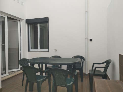 Möblierte Terrasse des Hostels Furnaka Village in Lourinhã mit dunkelgrünem Tisch und Stühlen vor weißen Wänden