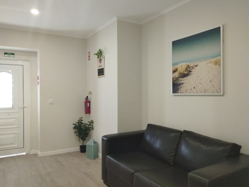 Moderner Hostel-Gemeinschaftsbereich mit schwarzem Lederssofa, beigen Wänden, Strandlandschaftskunst und Eingangstür