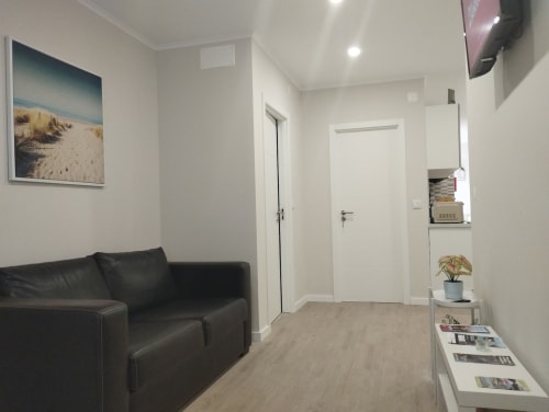 Modernes Hostel-Wohnzimmer mit schwarzem Ledersofa, weißen Türen, Holzboden und Strandkunst bei Furnaka