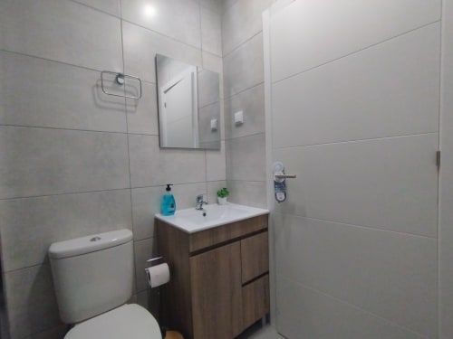 Modernes Badezimmer in der Furnaka Village Herberge in Lourinhã mit Holzwaschbecken, weißem Waschbecken, Toilette und gefliester Duschbereich