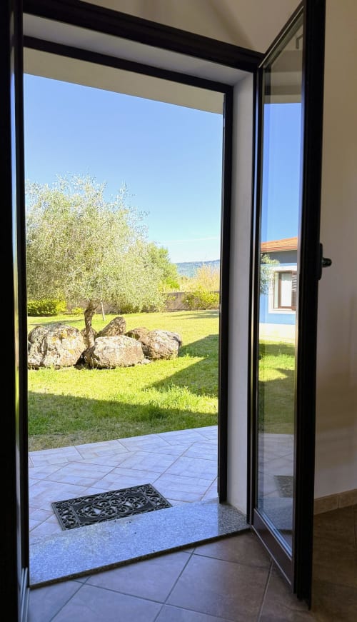 Porte in vetro aperte dell'Appartamento 3 che rivelano il giardino soleggiato con ulivi e dettagli in pietra di A Mare Case Vacanze,