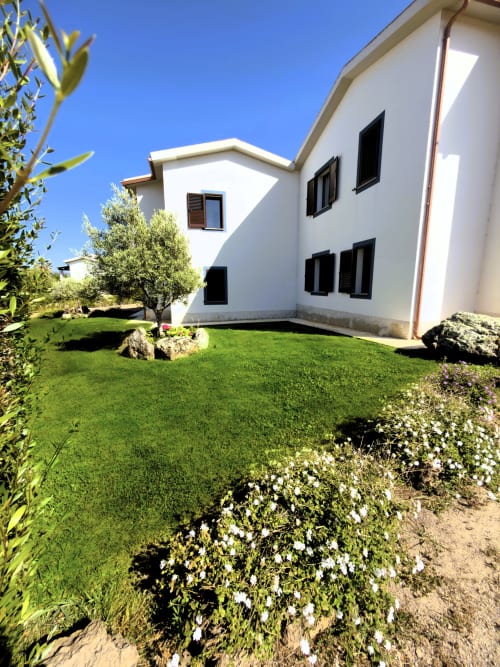 Moderno appartamento bianco con prato verde, ulivi e giardino fiorito presso A Mare Case Vacanze a Valledoria, Italia