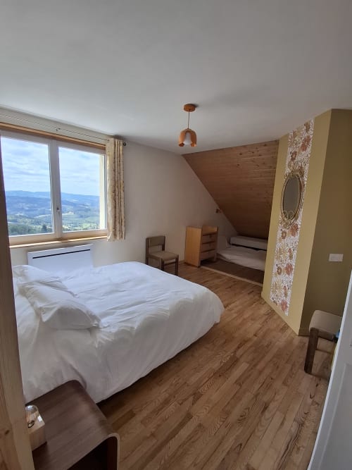 Spacious bedroom with mountain view at La Maison de Dun BnB, Saint Racho. Queen bed, wooden floors, mezzanine area.