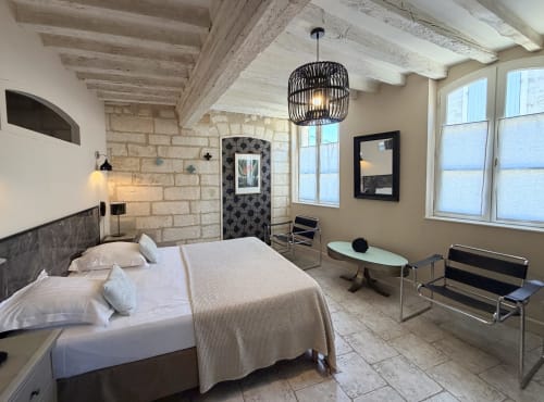 Chambre moderne à l'Hôtel La Suite à Villeneuve-lès-Avignon avec lit, murs en pierre, poutres apparentes et vue sur la ville