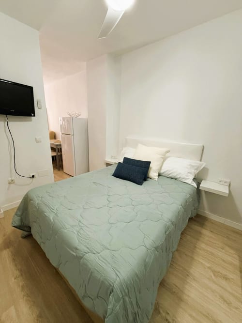 Luminoso dormitorio de apartamento estudio en Fuengirola con cama queen, TV, paredes blancas y suelo de madera