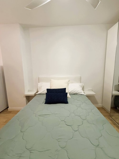 Moderno estudio junto al mar en Fuengirola con cama de matrimonio, mesitas blancas, almohada azul oscuro y decoración minimalista