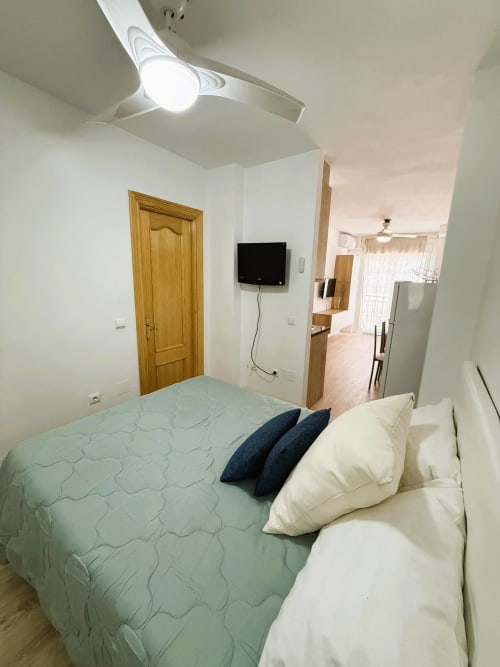 Acogedor estudio frente al mar en Fuengirola con cama, TV, almohadas blancas y ventilador de techo moderno