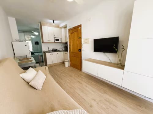 Moderno apartamento estudio en Fuengirola con cocina equipada, televisor de pantalla plana, suelos de madera y muebles blancos