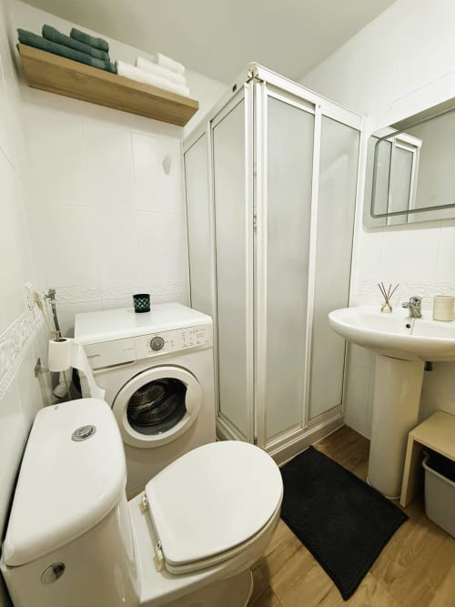 Baño moderno en estudio frente al mar en Fuengirola con ducha, inodoro, lavabo y lavadora-secadora integrada