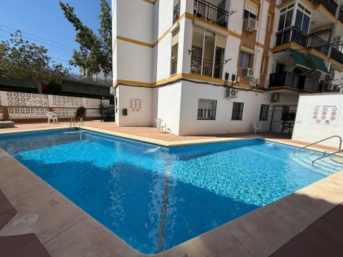 Soleada zona de piscina de apartamento en primera línea de playa Fuengirola, con edificio blanco y terraza de barro cocido