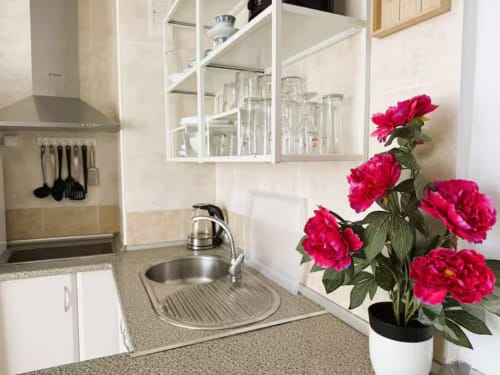 Cocina moderna con encimeras de granito, muebles blancos, fregadero de acero inoxidable y flores rosas vibrantes en la soleada playa de Fuengirola