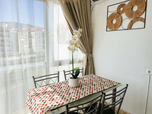 Comedor luminoso de apartamento frente al mar en Fuengirola con mesa, orquídeas y vistas a la ciudad