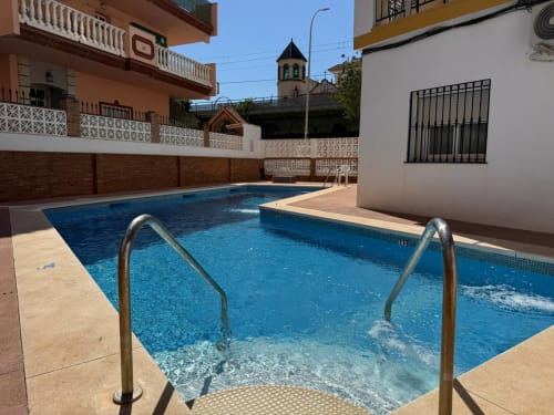 Piscina con barandillas metálicas en apartamento frente al mar en Fuengirola, España. Torre campanario visible al fondo.
