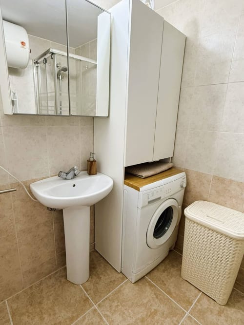 Baño moderno en apartamento frente al mar en Fuengirola con lavamanos, espejo botiquín, lavadora y cesto de mimbre