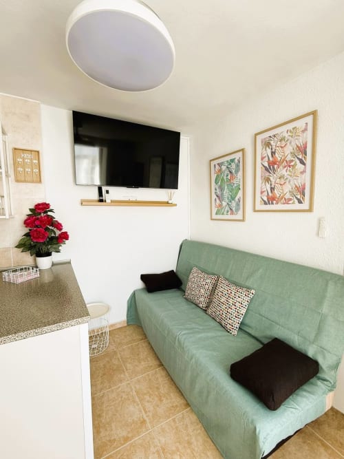 Apartamento soleado frente al mar en Fuengirola con sofá verde, cocina americana, TV y cuadros botánicos