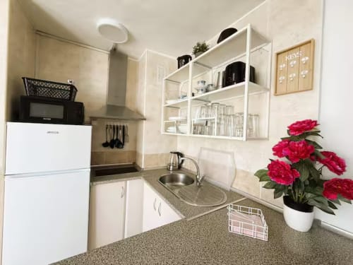 Cocina moderna de apartamento frente al mar en Fuengirola con muebles blancos, encimeras de granito, estantes y flores rojas