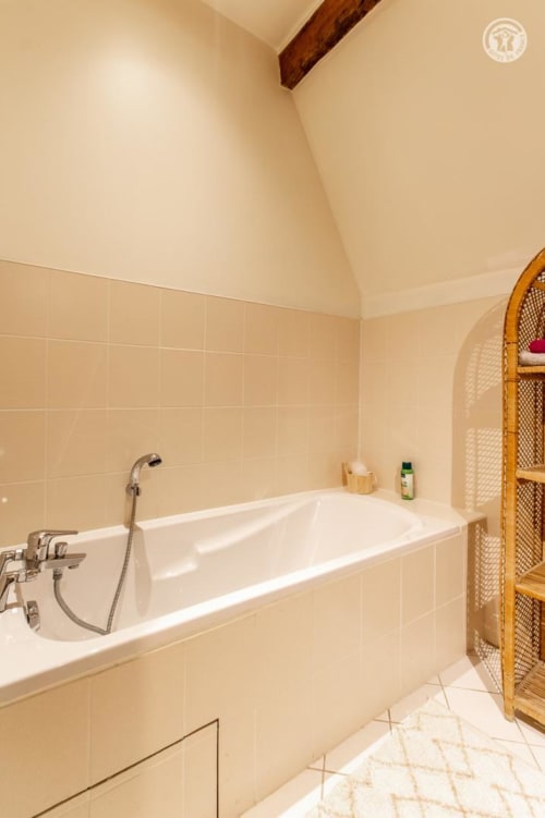 Salle de bain spacieuse avec baignoire blanche, murs carrelés et étagères en bois à Ô 3 Cyprès de Précy
