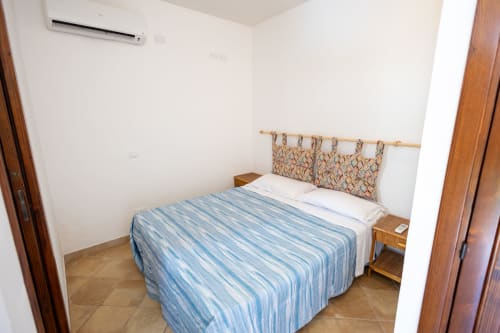 Camera luminosa dell'appartamento Emily in Sicily a San Vito Lo Capo, con letto a righe blu e testiera in legno